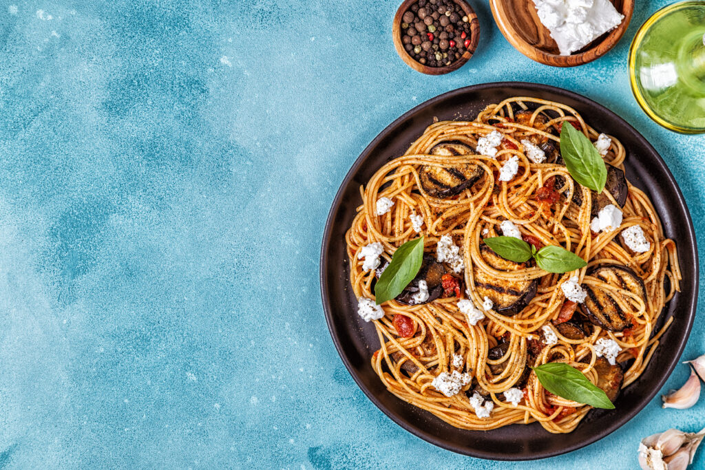 Pasta alla Norma - traditional Italian food with eggplant, tomato, cheese and basil, top view.