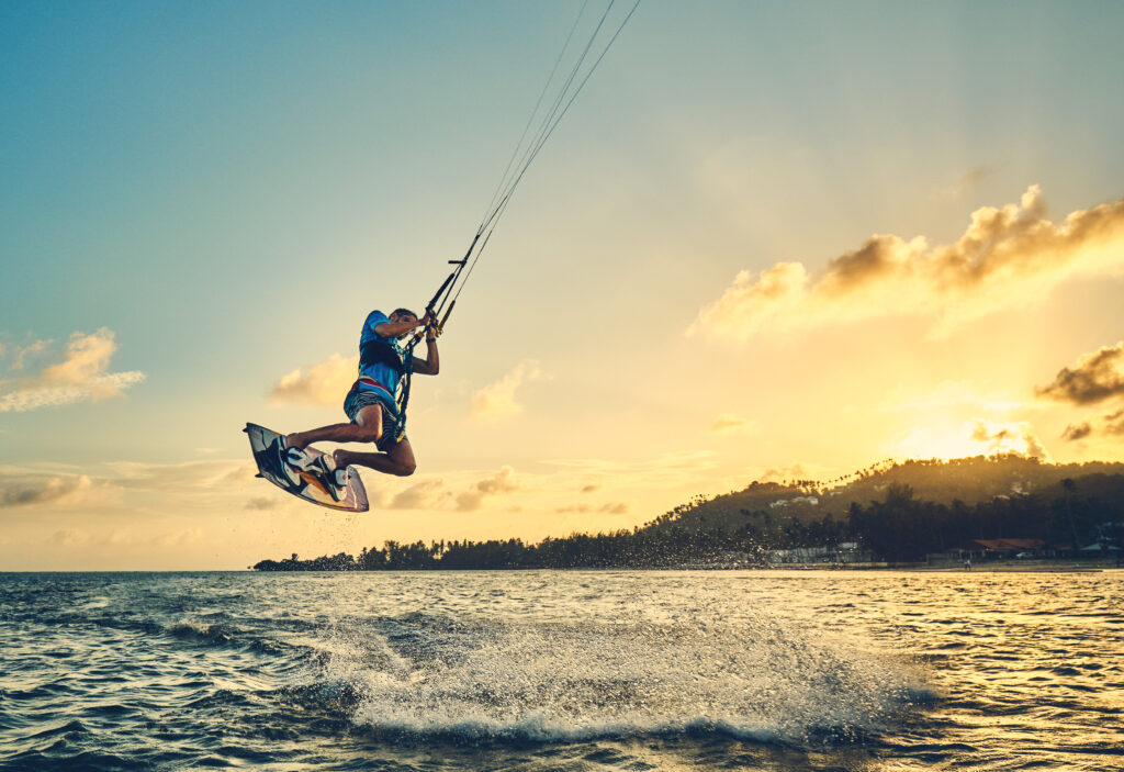 Young man kite boarder jumps over the sea at sunset