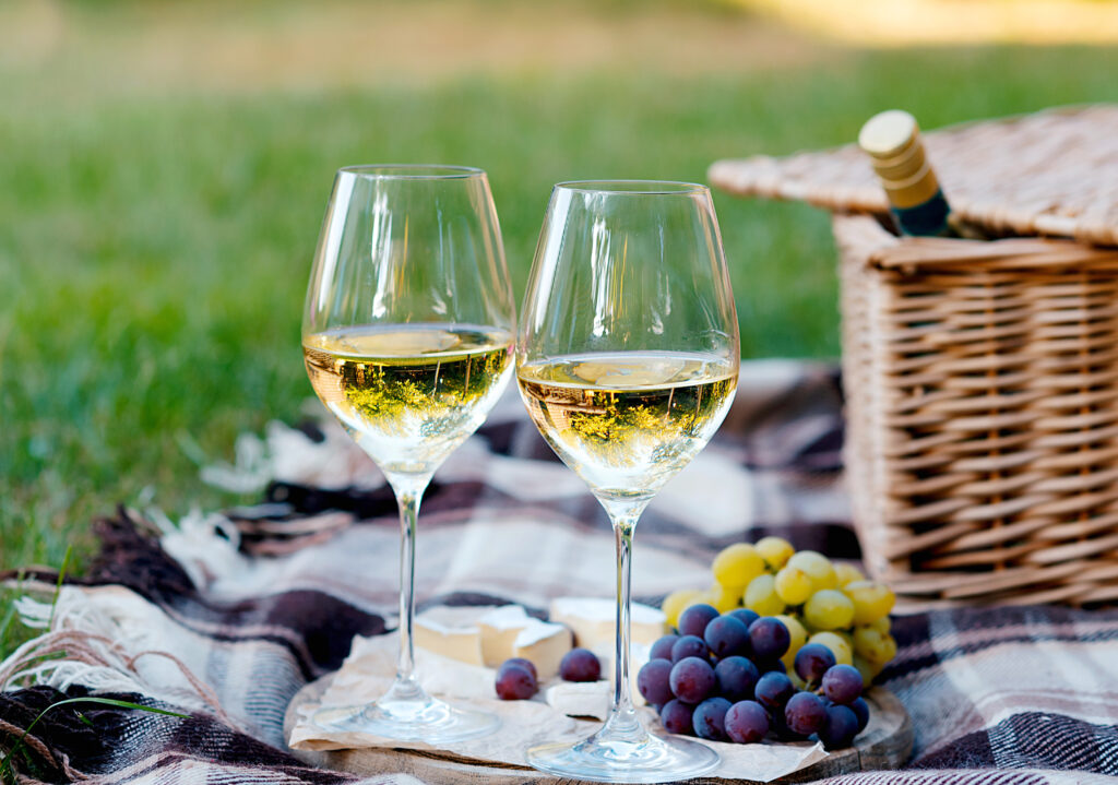 Two glasses of white wine and a wooden plate with cheese and grapes served outside